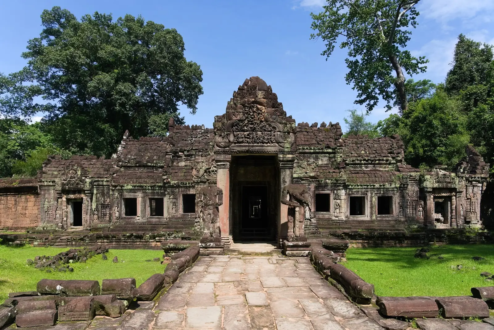 The stone entrance gateway of Preah Khan temple beyond a paved causeway, surrounded by trees